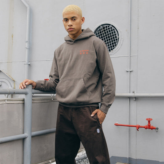 Man wearing the taupe Eminem Kamikaze x Standard Issue hoodie with orange chest print