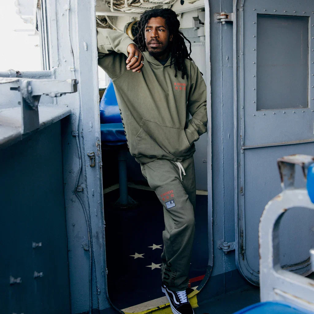 Model in burnt olive Eminem Kamikaze x Standard Issue sweatpants in a ship doorway