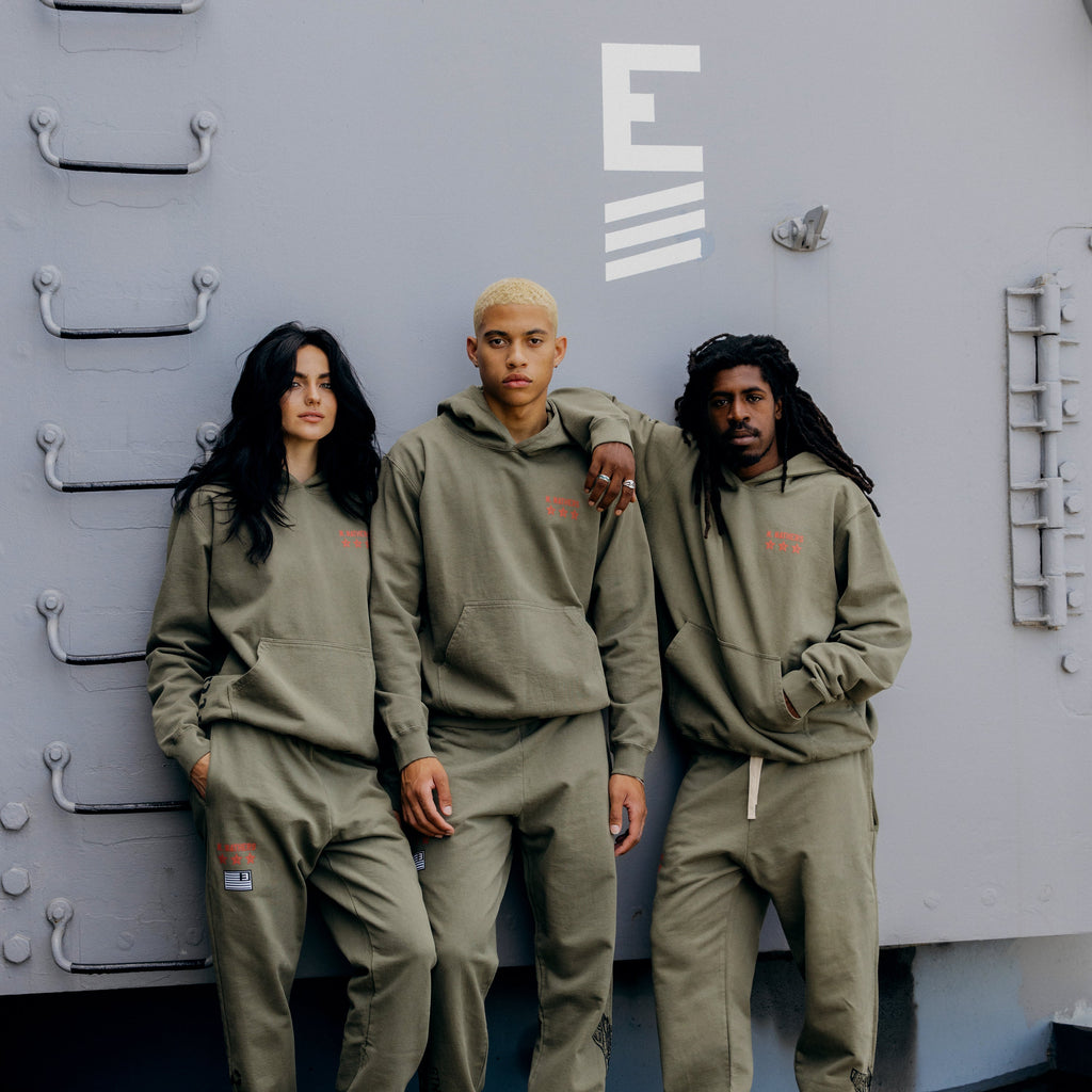 Three models in burnt olive Eminem Kamikaze x Standard Issue hoodies on a ship deck