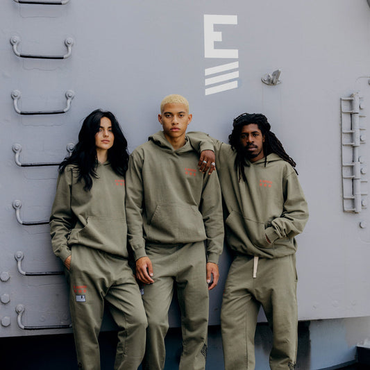 Three models in burnt olive Eminem Kamikaze x Standard Issue hoodies on a ship deck