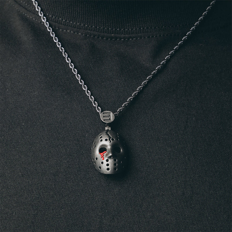 Eminem hockey mask pendant close-up on a silver chain against dark fabric