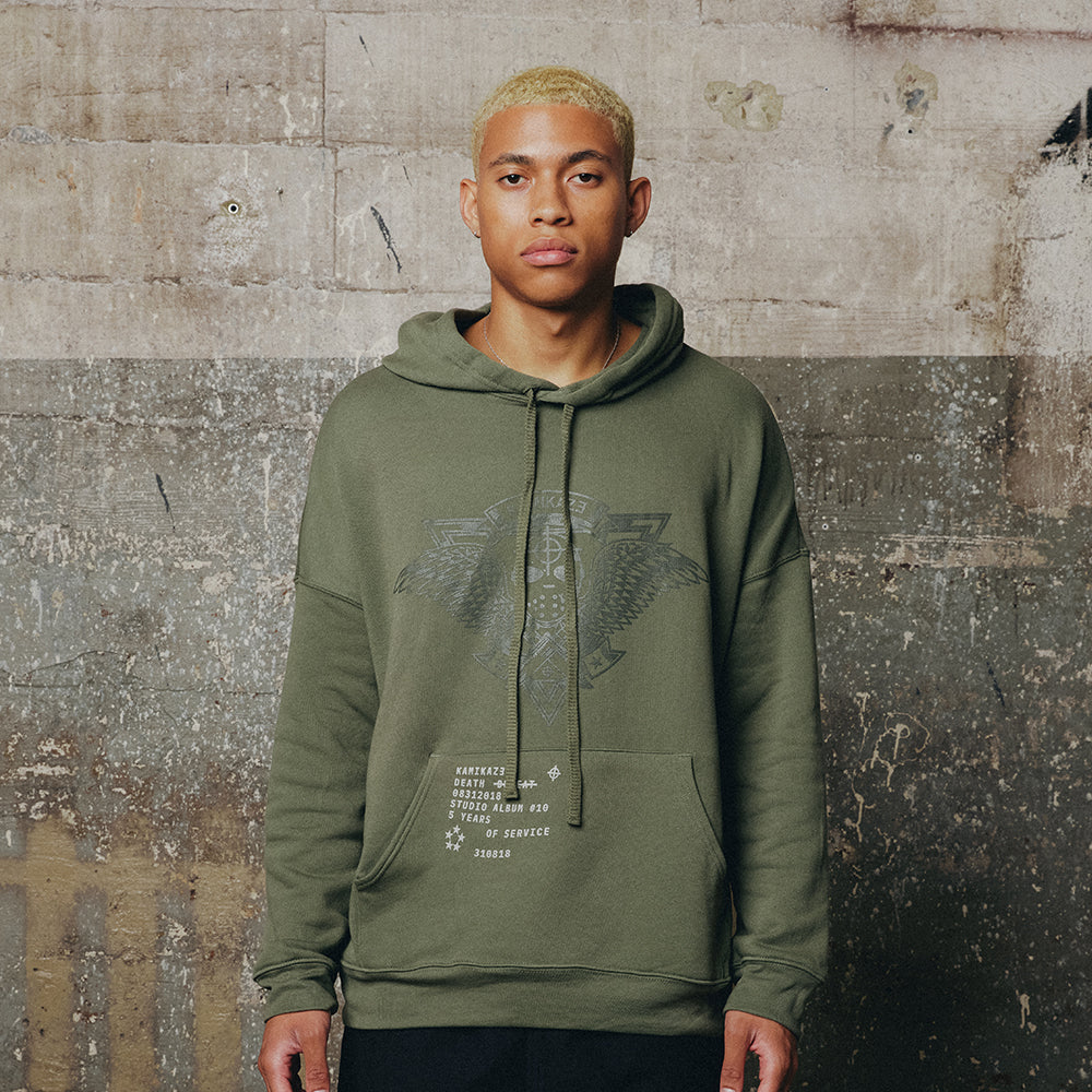 Man wearing the olive green Eminem Kamikaze Crest hoodie with tonal crest print