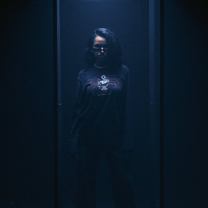 Model in the black Eminem Recovery Tracklist long sleeve in a dark blue-lit room