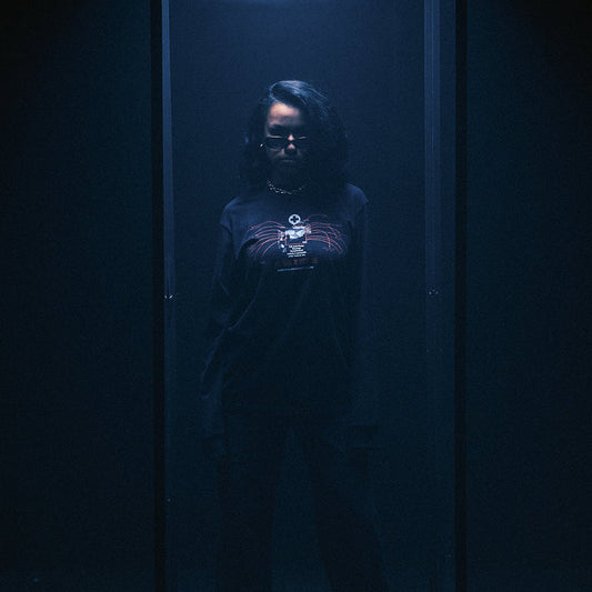 Model in the black Eminem Recovery Tracklist long sleeve in a dark blue-lit room