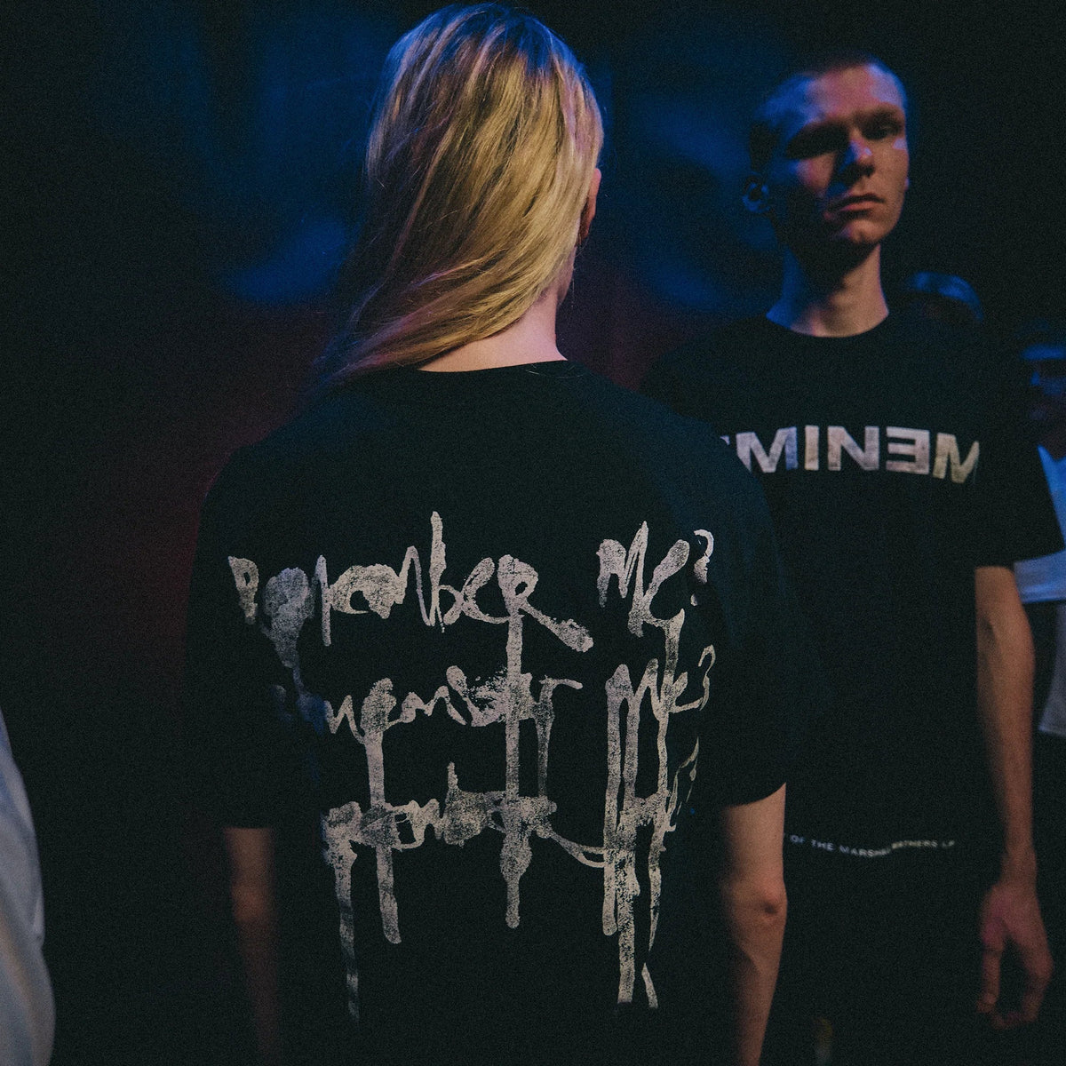 Two models in black Eminem MMLP25 Remember Me T-shirts under blue stage lighting