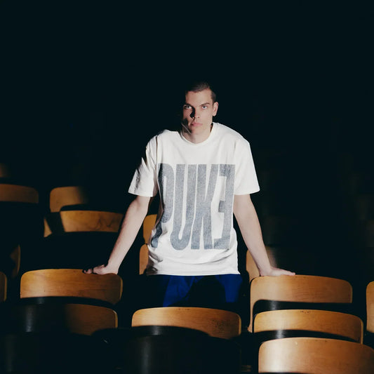 Man wearing the white Eminem Encore PUKE T-shirt in a theatre auditorium