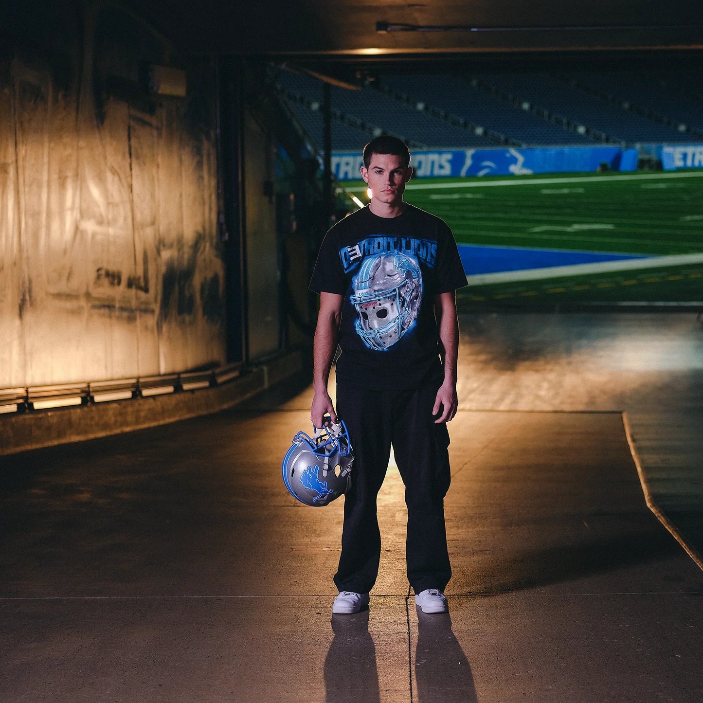 Model holding a Detroit Lions helmet in the Eminem All Grit T-shirt in the stadium tunnel