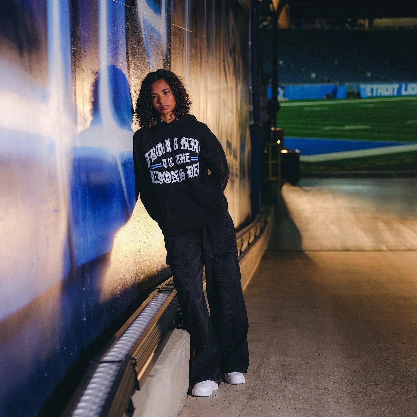 Model in the black Eminem x Detroit Lions Helmet hoodie in the stadium concourse