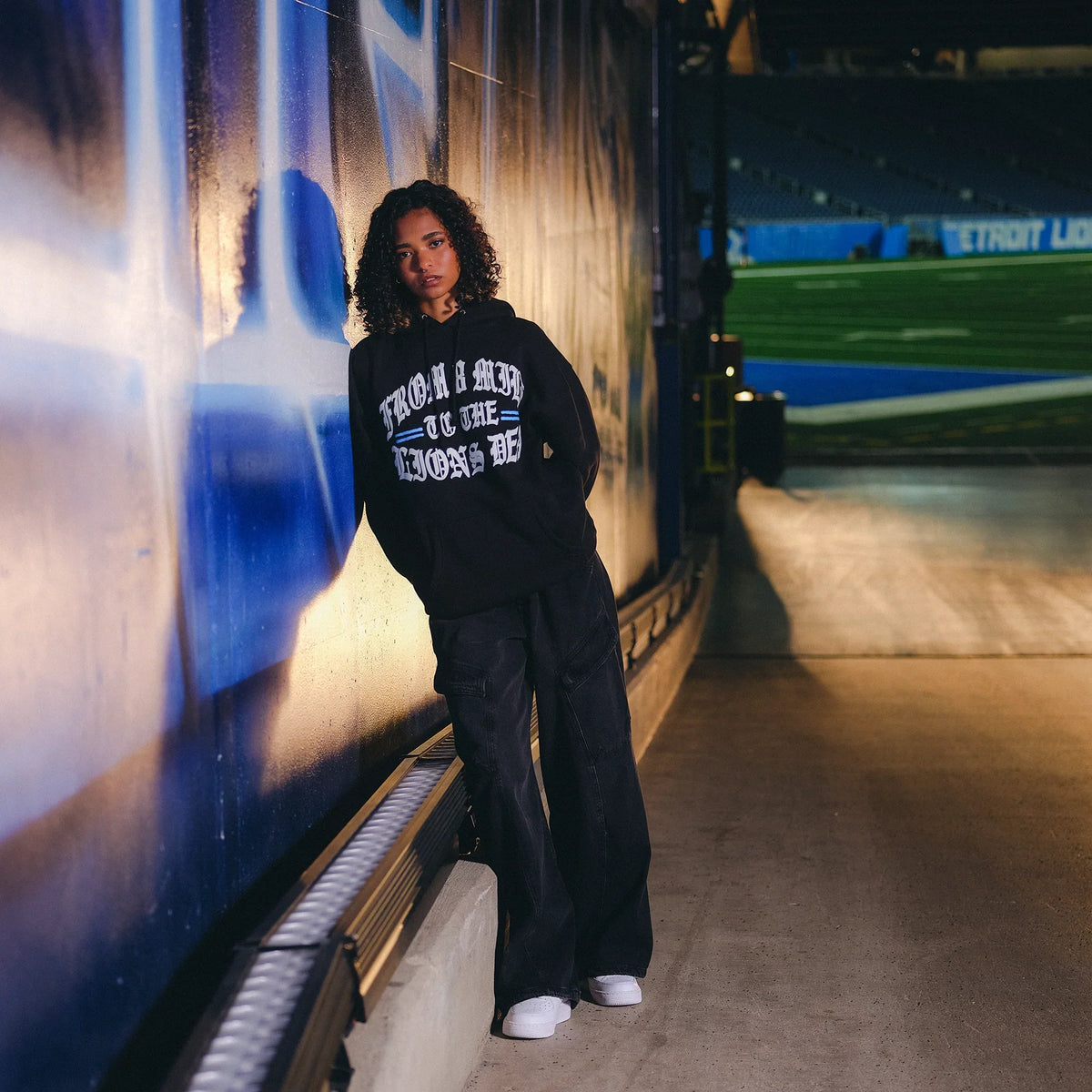 Model in the black Eminem x Detroit Lions Helmet hoodie in the stadium concourse