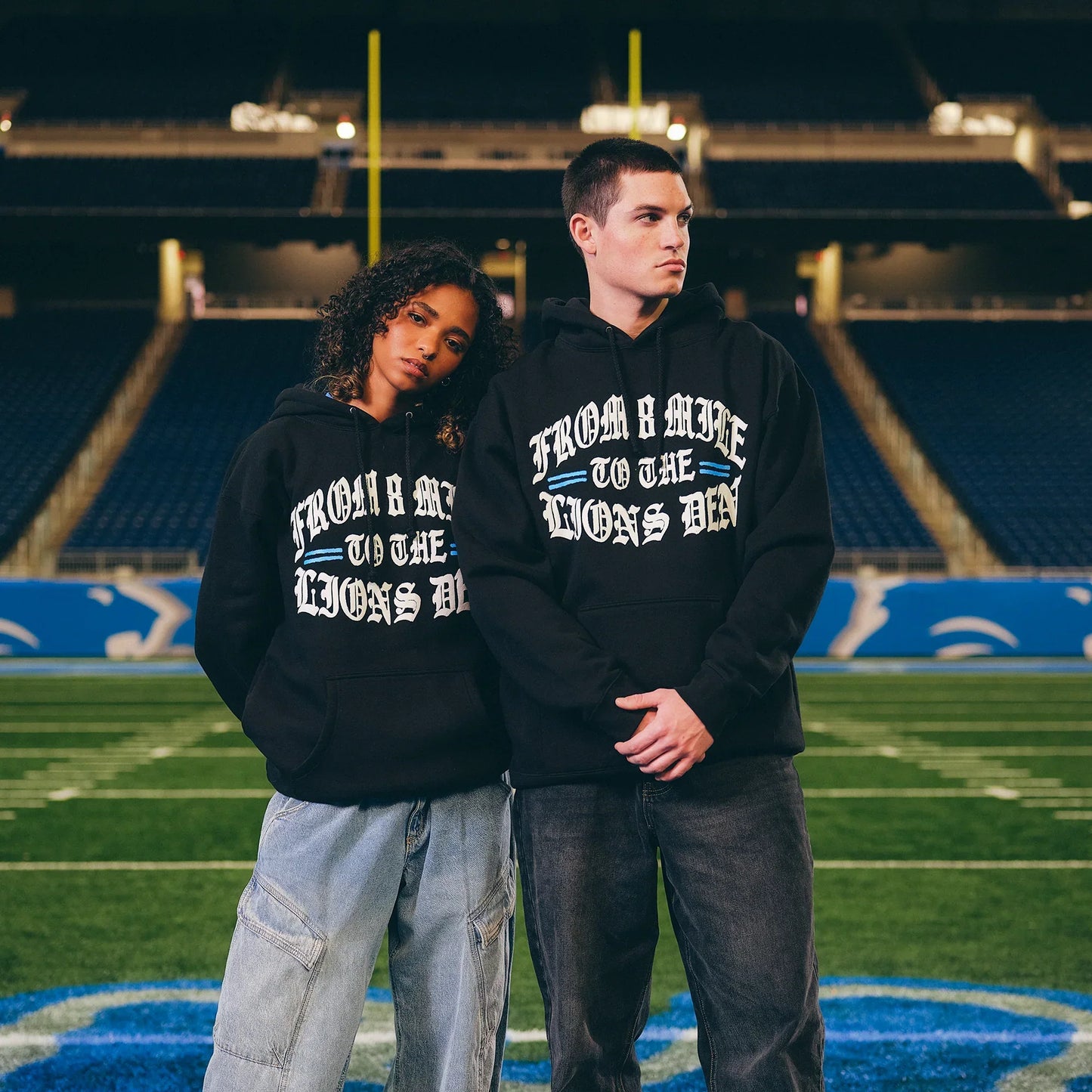 Two models in Eminem x Detroit Lions Helmet hoodies on the field at Ford Field
