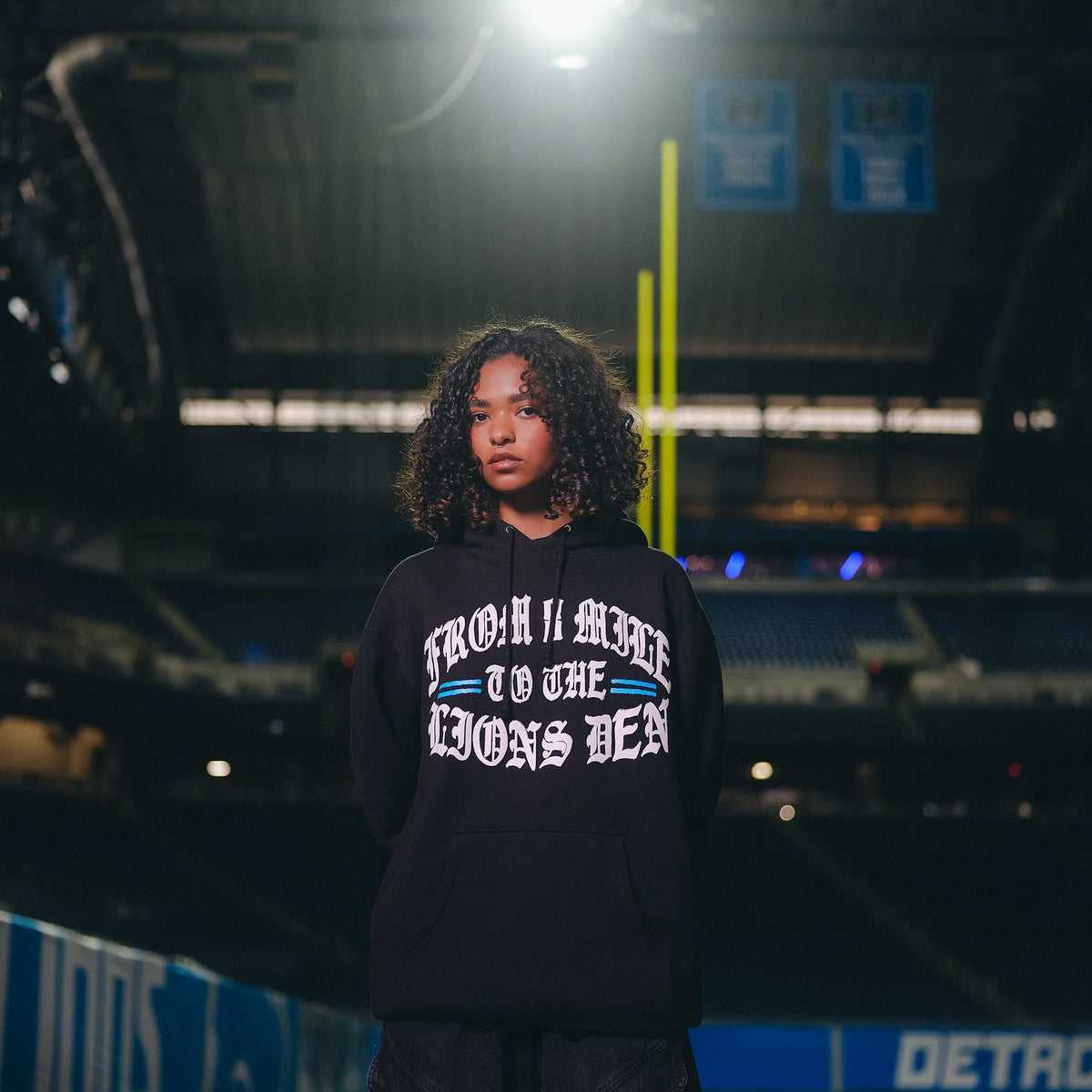 Woman wearing the black Eminem x Detroit Lions hoodie on the field at night