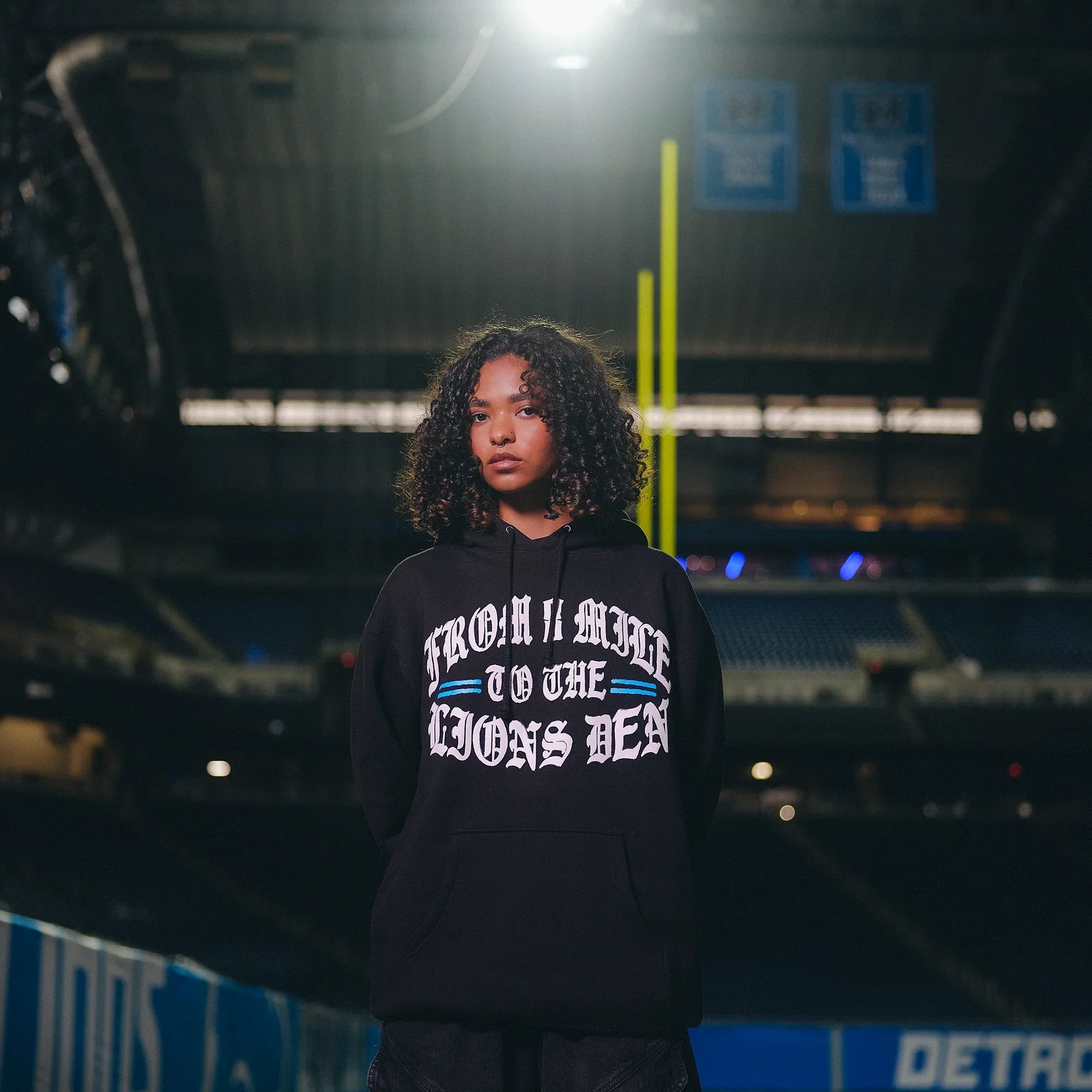 Woman wearing the black Eminem x Detroit Lions hoodie on the field at night