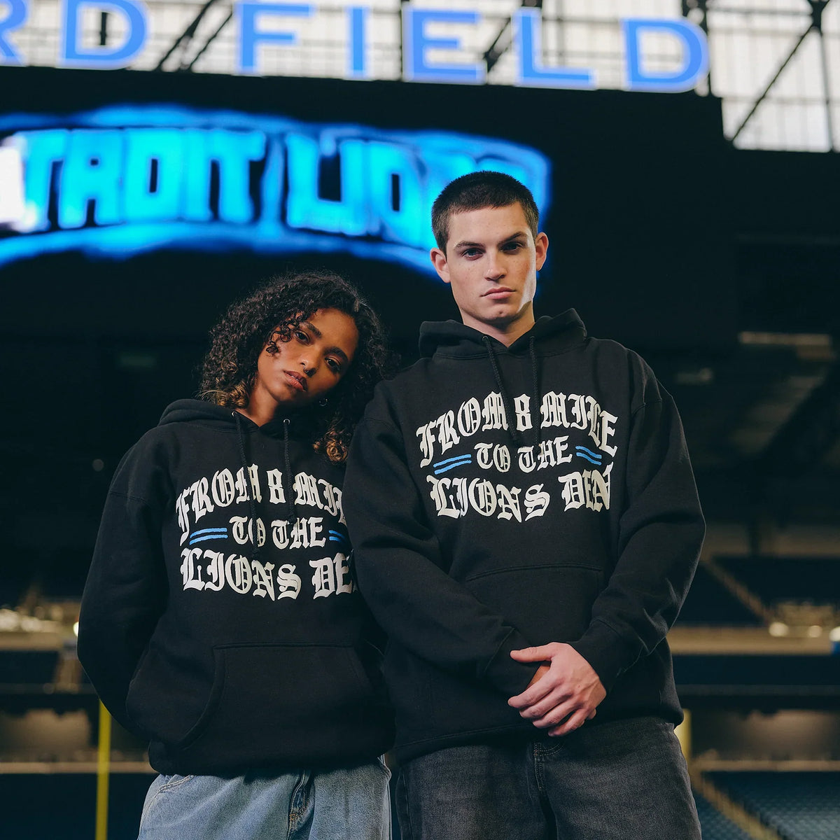 Two models in black Eminem x Detroit Lions Helmet hoodies under stadium lights