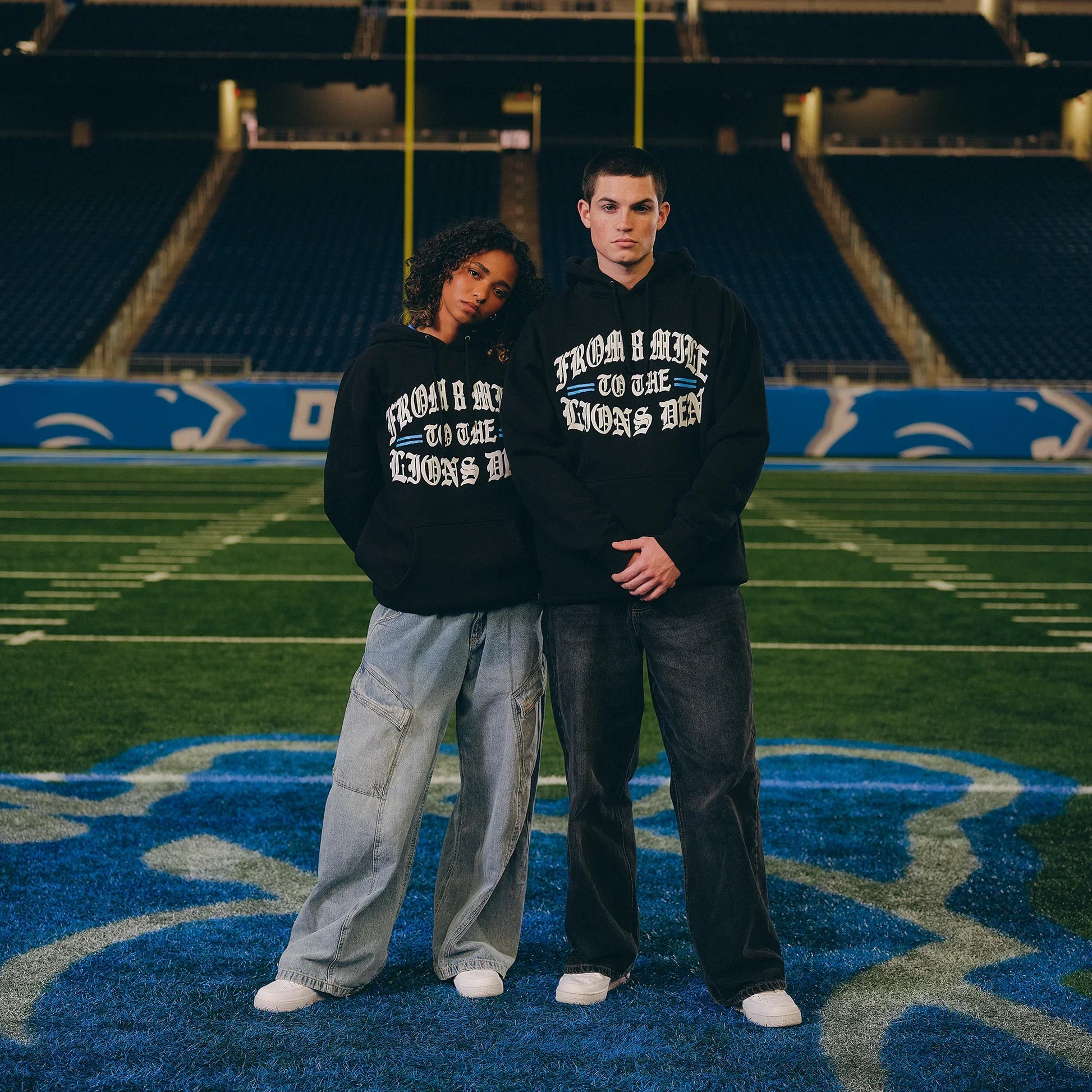 Full-length view of two models in Eminem x Detroit Lions Helmet hoodies on the pitch