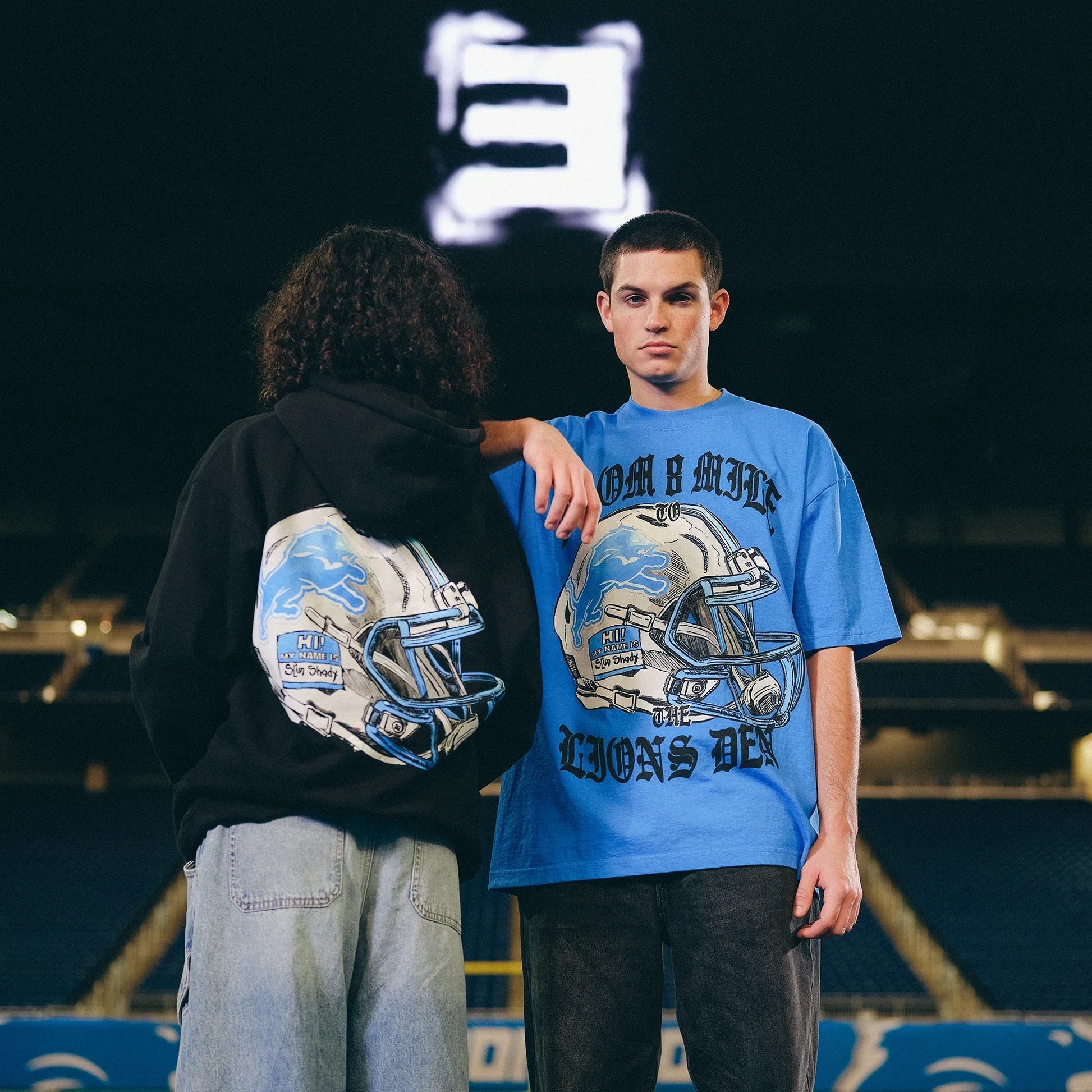 Models in Eminem x Detroit Lions Helmet tee and hoodie showing front and back helmet prints