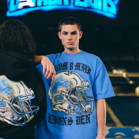 Man in the blue Eminem x Detroit Lions Helmet T-shirt with chrome helmet and Lions Den print
