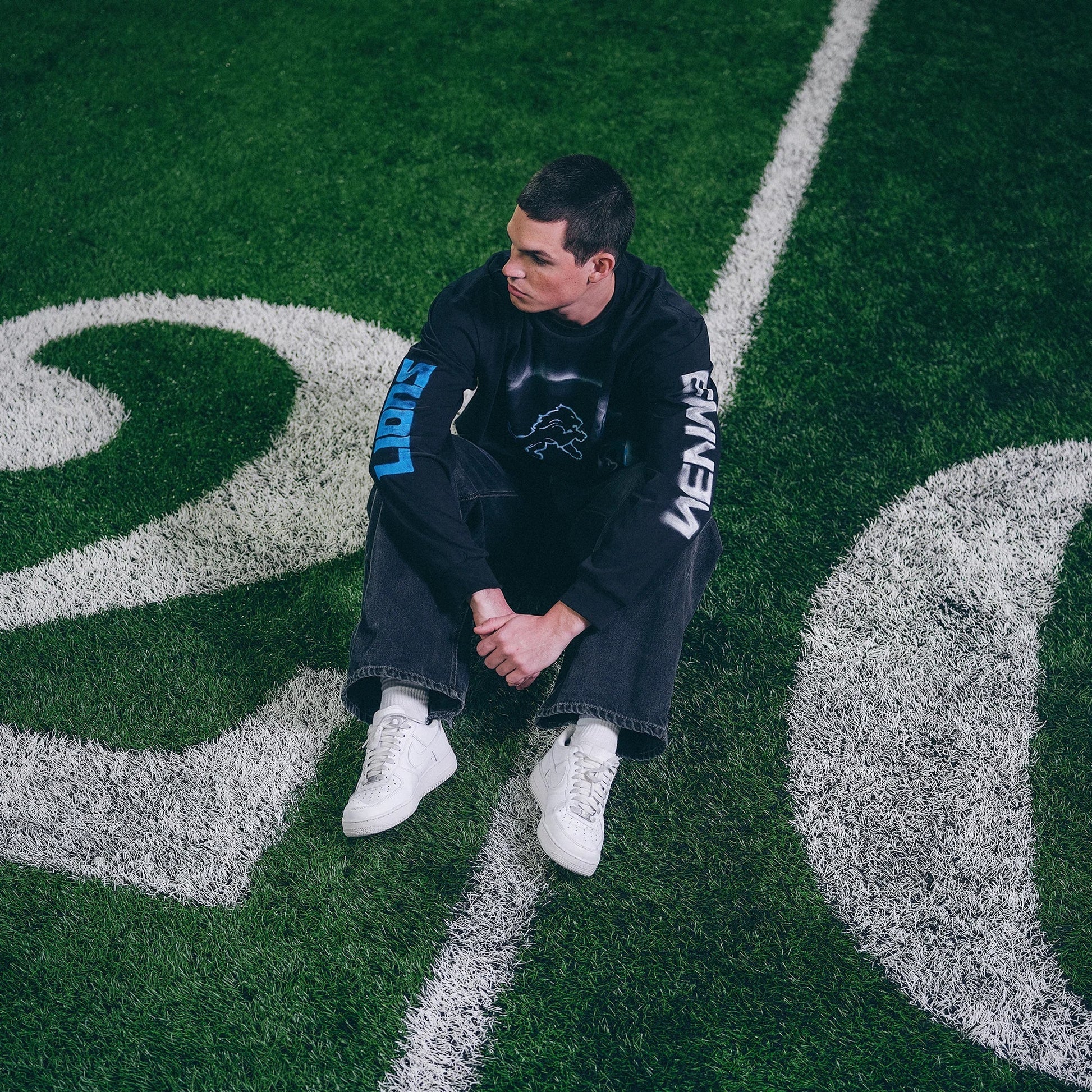 Model crouching in the Eminem x Detroit Lions Silhouette long sleeve on the yard markings
