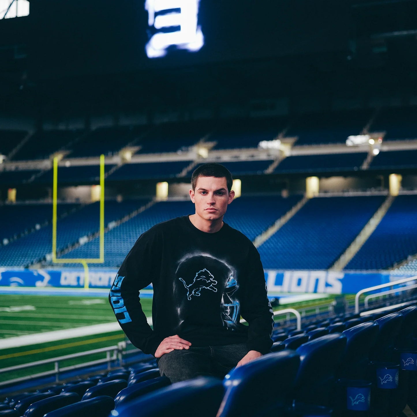 Man in the black Eminem x Detroit Lions Silhouette long sleeve seated in the stadium stands