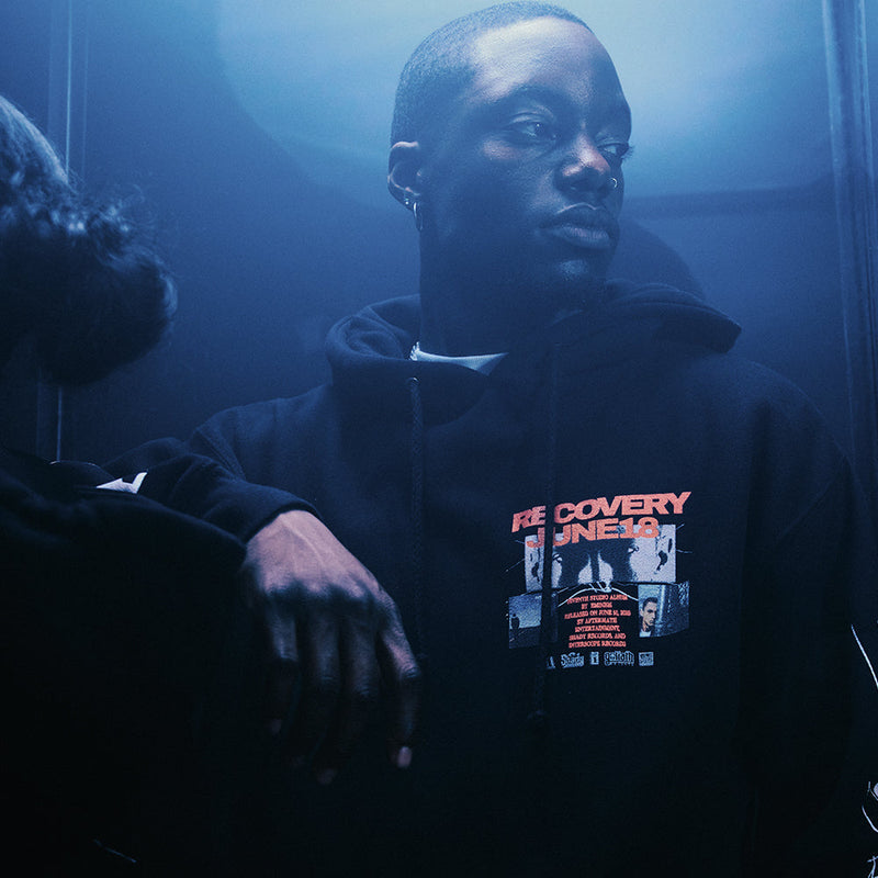 Man wearing the black Eminem Recovery 15th Anniversary hoodie with collage chest print