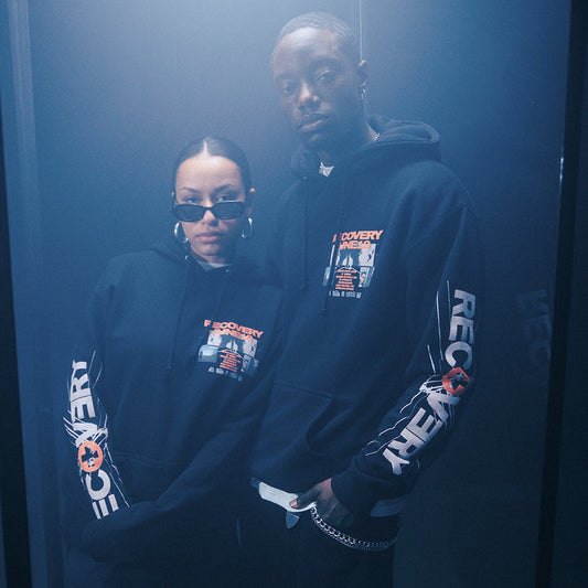Two models in black Eminem Recovery 15th Anniversary Collage hoodies in blue light