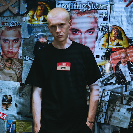 Man wearing the black Eminem Hi My Name Is Stan T-shirt against a magazine-covered wall