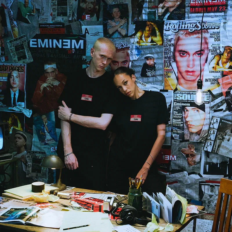 Two models in black Eminem Hi My Name Is Stan T-shirts in a magazine-walled room