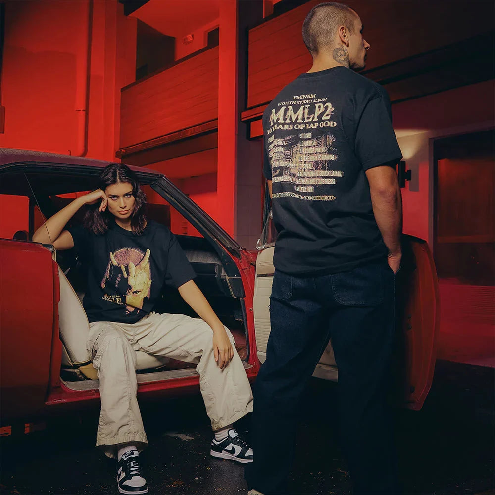 Two models in black Eminem MMLP2 Horns T-shirts in a red-lit motel corridor