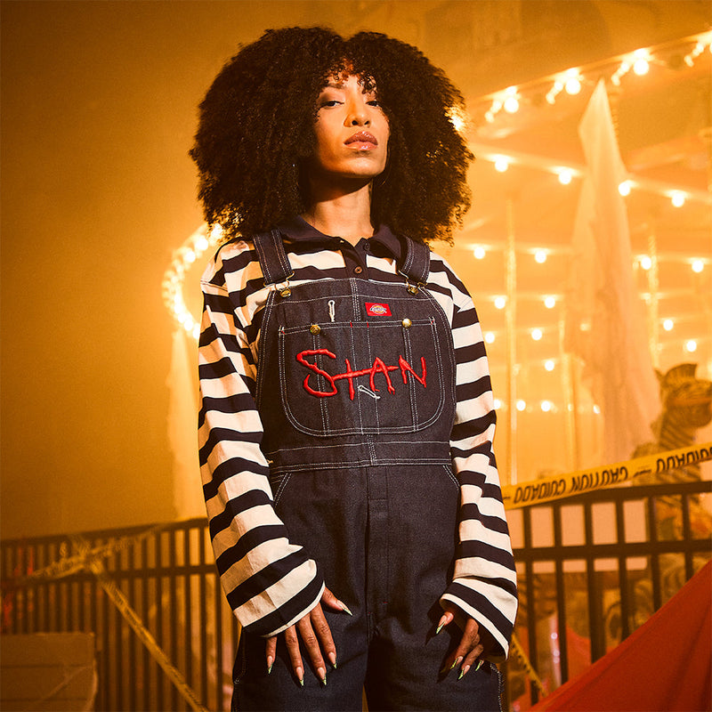 Woman wearing the Eminem Stan denim overalls over a striped long sleeve