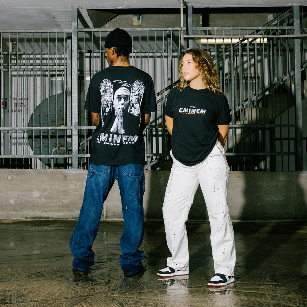 Two models in black Eminem Show Stained Glass T-shirts against a metal gate