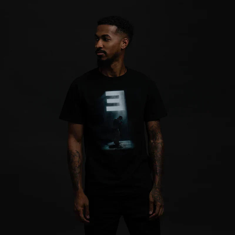 Man wearing the black Eminem Stage Lights graphic T-shirt with glowing E logo print