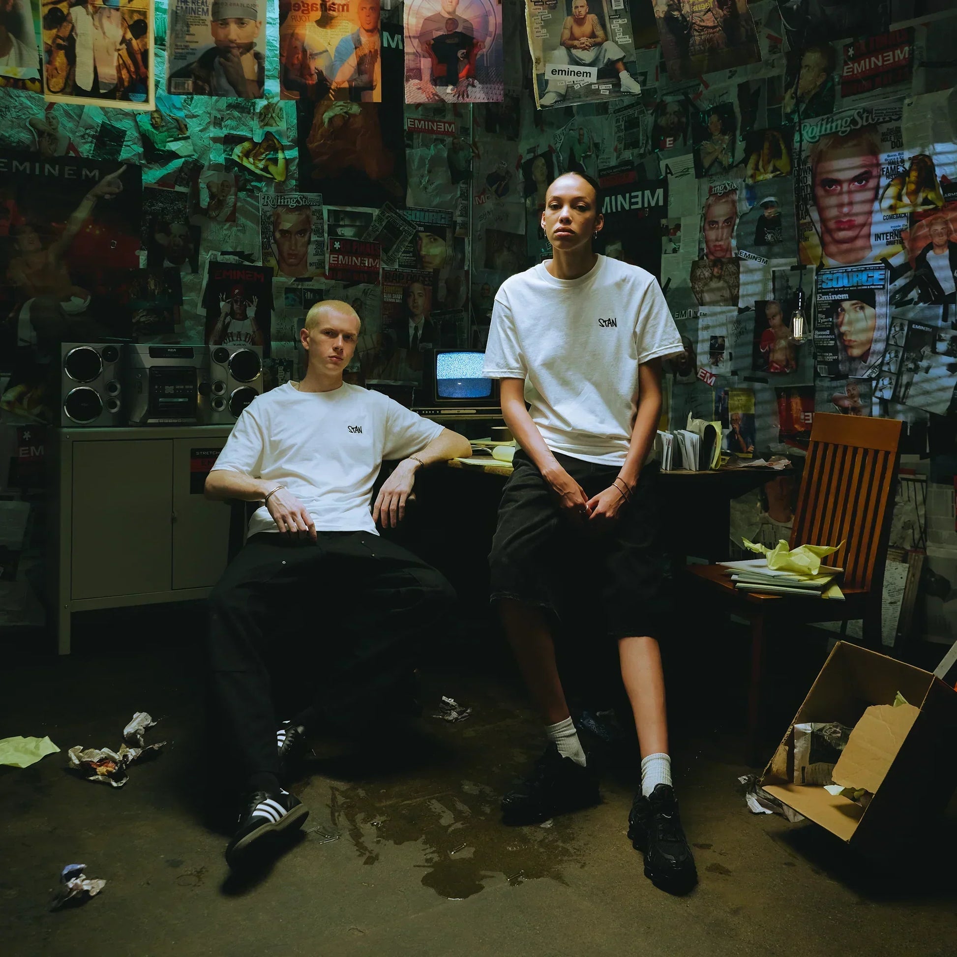 Two models in white Eminem Stan embroidered T-shirts against a magazine-covered wall