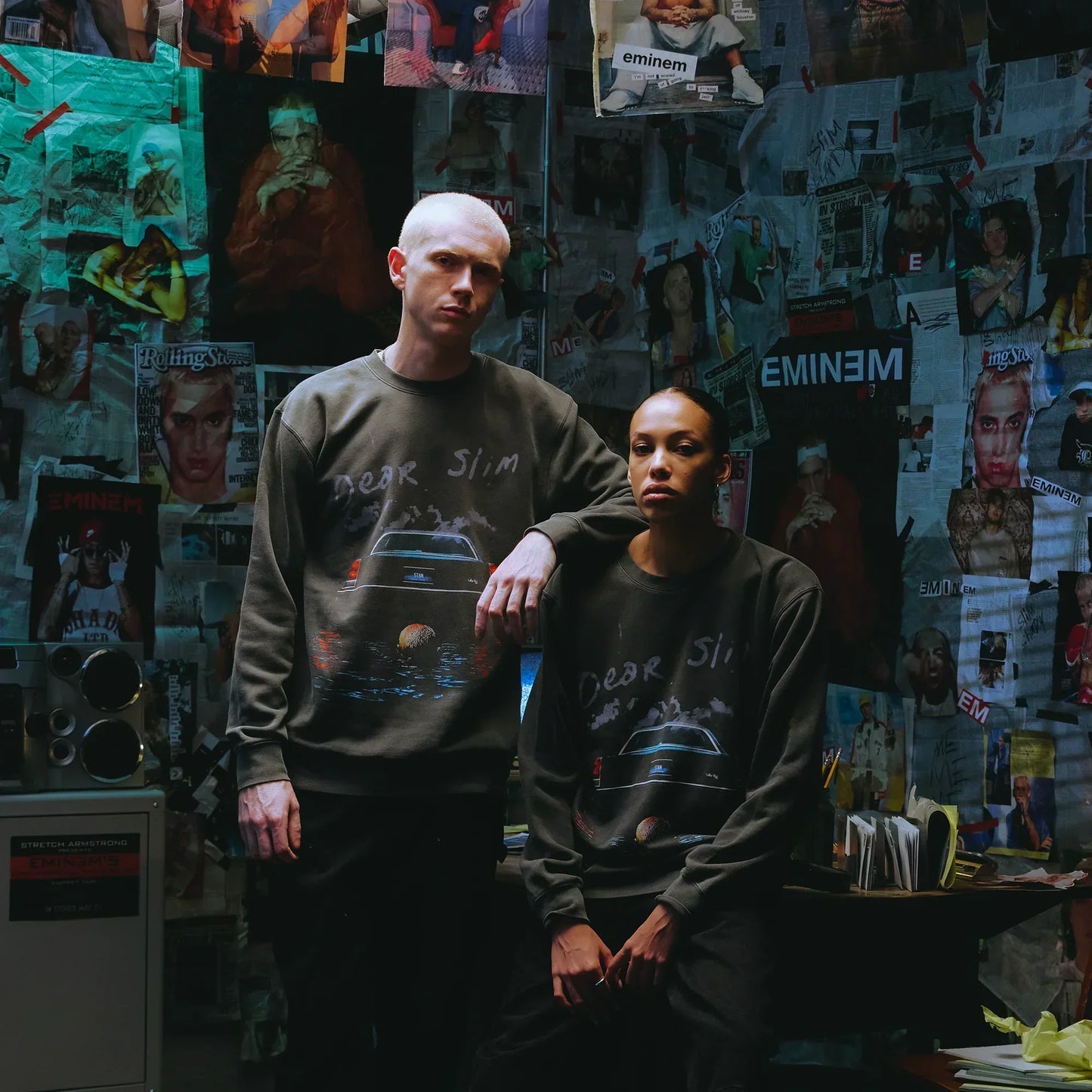 Two models in Eminem Dear Slim crewneck sweatshirts against a magazine-covered wall