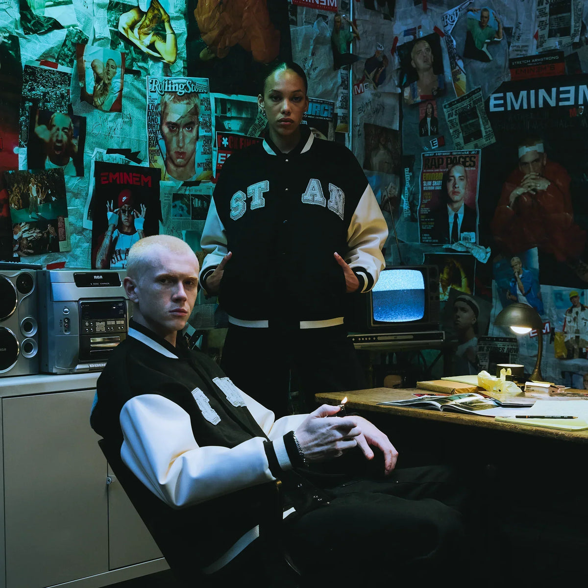 Two models in Eminem Stan varsity jackets in a magazine-covered room