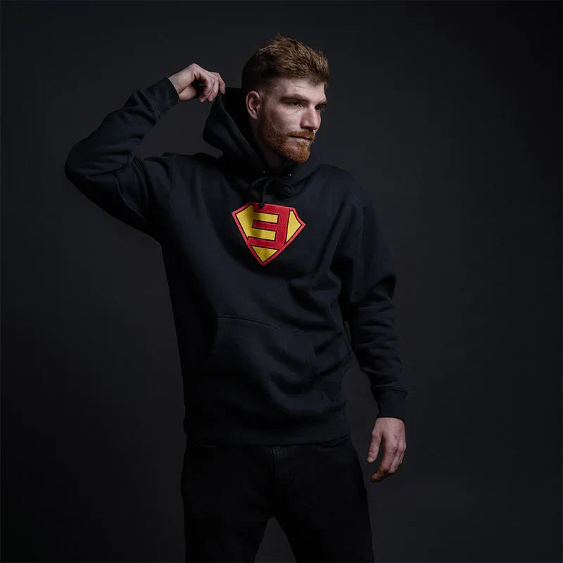 Man wearing the black Eminem Super-E logo hoodie with red and yellow shield chest print