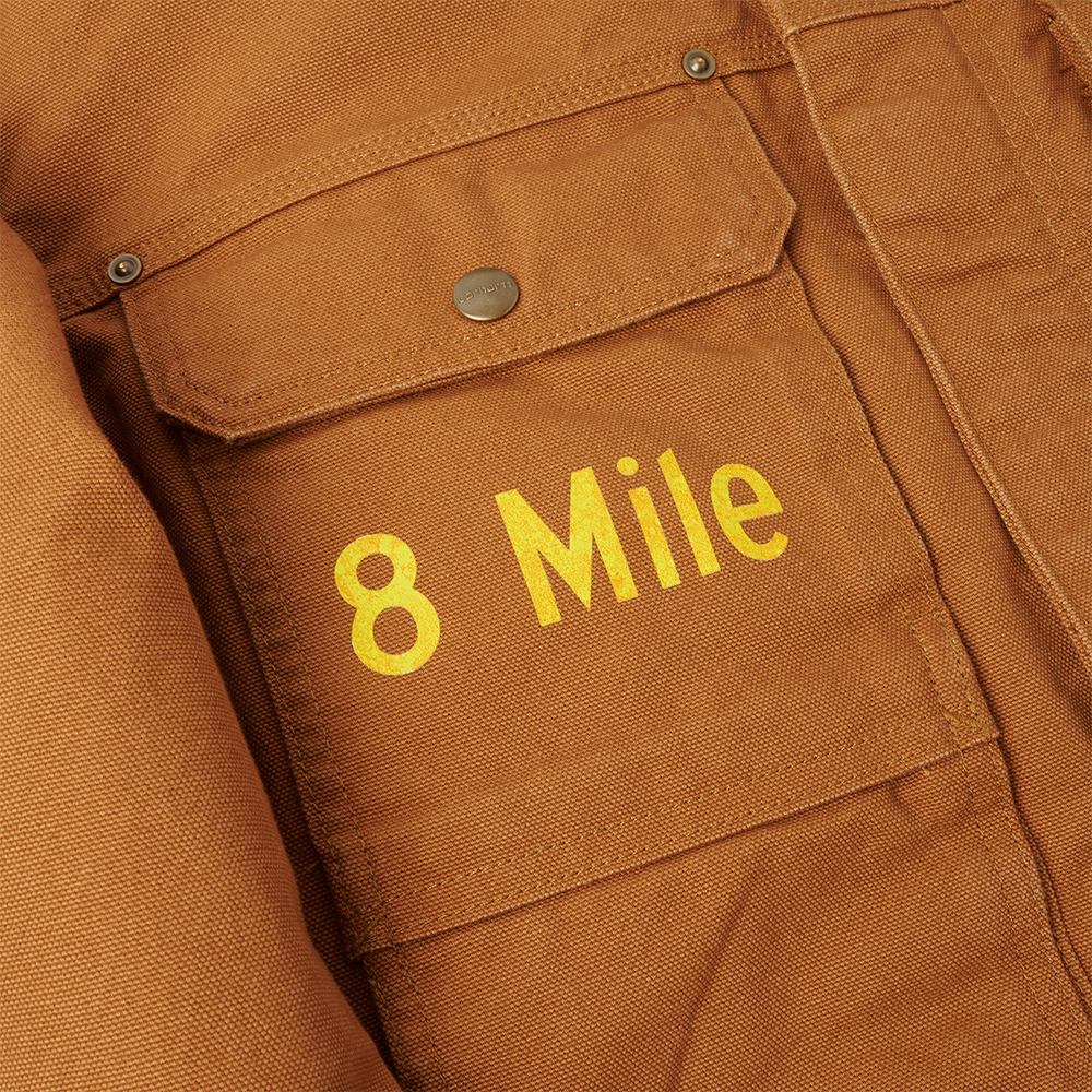 Close-up of yellow 8 Mile embroidery on the chest pocket of the brown Eminem Carhartt duck jacket