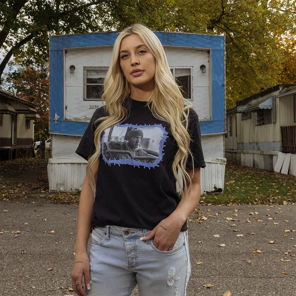 Woman in black Eminem 8 Mile Barbed Wire T-shirt, front photo print of a Detroit trailer home