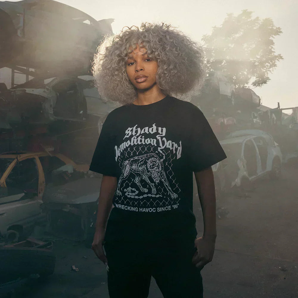 Woman wearing the black Eminem Shady Demolition Junkyard Dog T-shirt in a wrecking yard