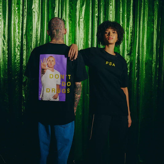 Two models in black Eminem SSLP25 PSA T-shirts against a green backdrop