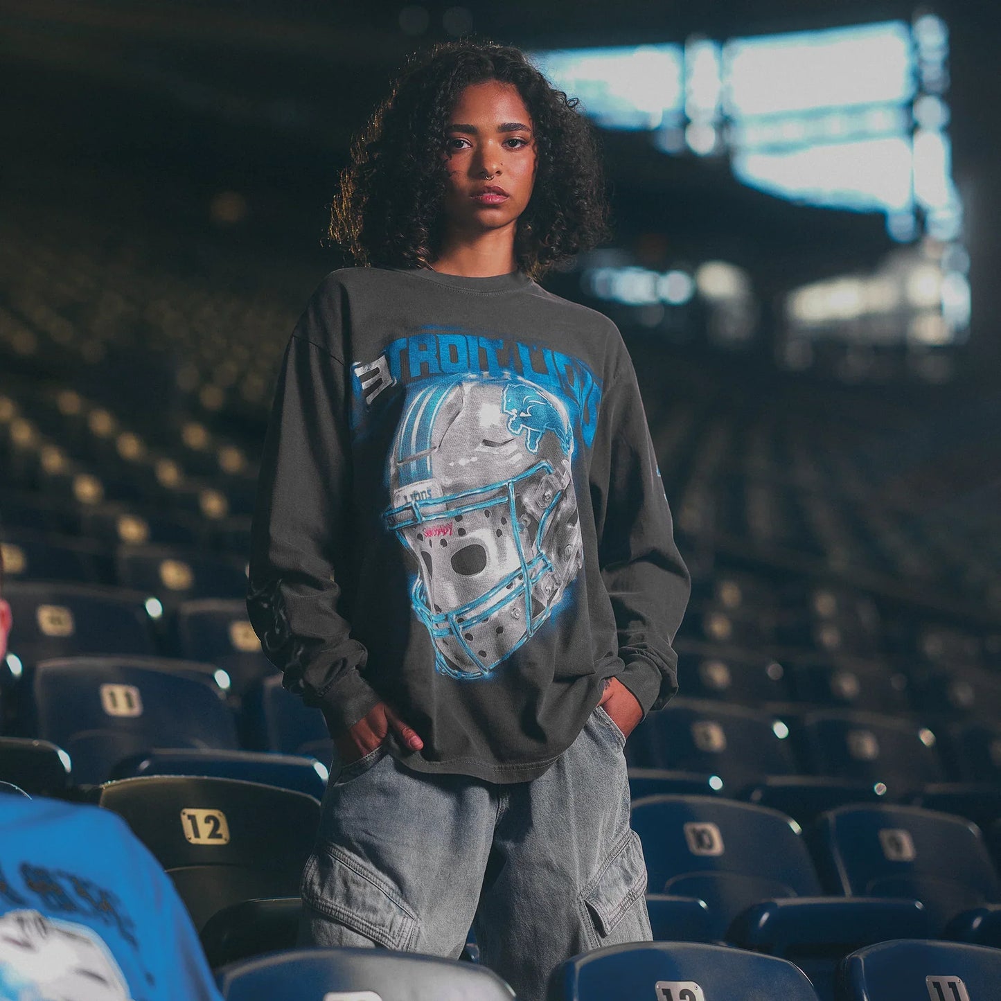 Model in the grey Eminem x Detroit Lions All Grit long sleeve seated in stadium seats
