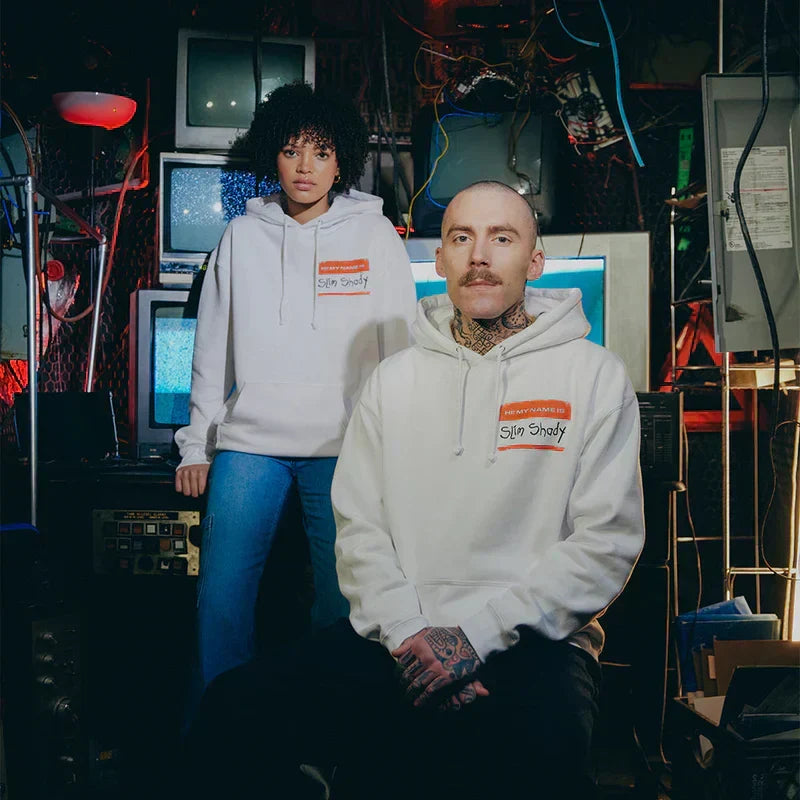 Models wearing white Eminem SSLP25 Name Tag hoodies in a neon-lit arcade
